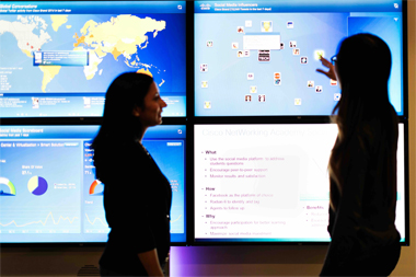 Dos mujeres delante de una pantalla con gráficos y mapas, explicando una presentación 