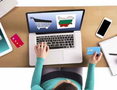 A laptop, tablet, and cellphone in various positions on top of a  desk with a person shopping online at Vibrant Versatility Co an e-commerce online shop that offers an immense variety of products. Show the desk with objects and person sitting & shopping